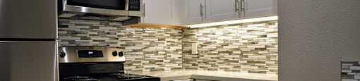 Kitchen with stainless appliances, tiled backsplash, and white cabinets
