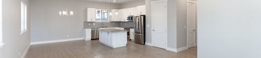 A spacious room with a ceiling fan and a kitchen area in the background.