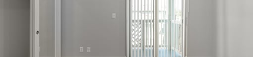 A room with a carpeted floor, a window with blinds, and a door.
