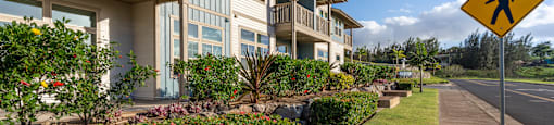 A pedestrian crossing sign is on the side of a road in front of a building with a well-maintained garden.