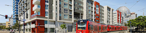 A red train is on the tracks in front of a modern building.