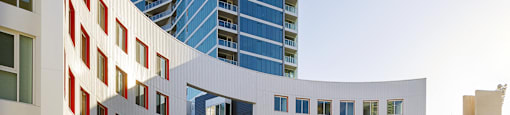 A modern building with a curved white section in front of a tall blue building.