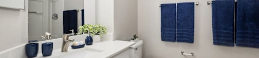 A white bathroom with a toilet, sink, and blue towels.