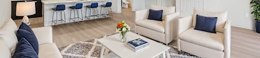 A modern living room with a white sofa, a coffee table, and a kitchen area in the background.