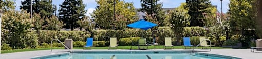 a swimming pool with a blue umbrella and chairs around it