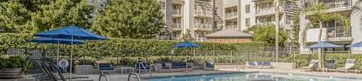 a swimming pool with chairs and umbrellas in front of an apartment building