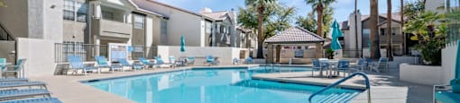 A swimming pool surrounded by sun loungers and palm trees.