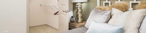 A bedroom with a bed, lamp, and a closet with clothes hanging.