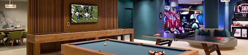A pool table is in the middle of a room with a TV and a bar.