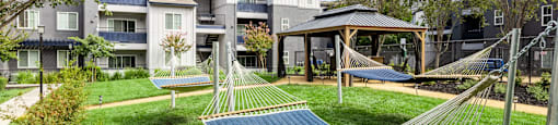 a yard with hammocks and a gazebo in front of an apartment