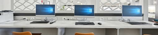 Three computers are on a white desk with orange chairs.