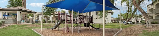 a playground with a swing set and a blue umbrella