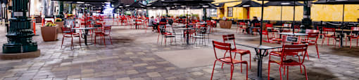 a plaza at night with red chairs and umbrellas and street lights