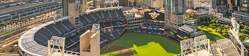 A large stadium with a green field in the center and a city skyline in the background.
