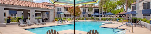 A pool with a striped umbrella and chairs.