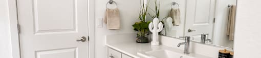 A white bathroom with a sink, mirror, and towel rack.