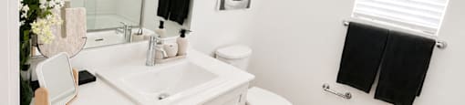A bathroom with a white toilet, sink, and a black and white rug.