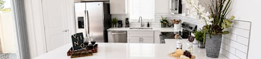 A kitchen with white cabinets and a white island with two stools.