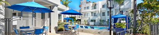 a patio with blue chairs and umbrellas and a swimming pool