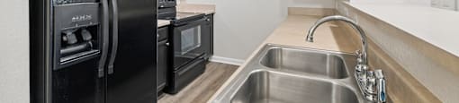 A black fridge and oven in a kitchen with a stainless steel sink.