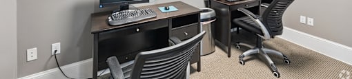 A room with two desks and chairs, one of which has a laptop and a monitor on it.