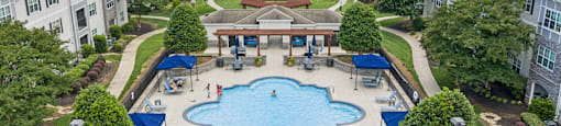 A swimming pool surrounded by trees and a building in the background.