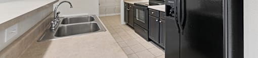 A black refrigerator is in the corner of a kitchen with white cabinets.