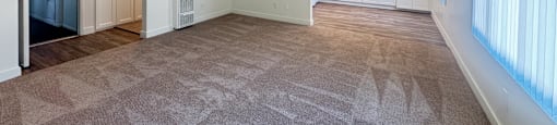 A spacious living room with a patterned carpet and a kitchen in the background.