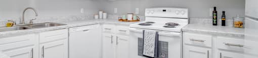 A white kitchen with a stove, sink, and cabinets.