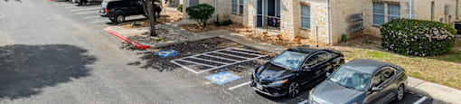 A black car is parked in a parking lot in front of a building.