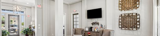 A living room with a grey couch, a coffee table, and a flat screen TV mounted on the wall.