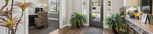 A well-lit hallway with a wooden floor and a variety of potted plants.