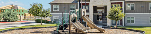 A playground with a slide in front of a two-story house.
