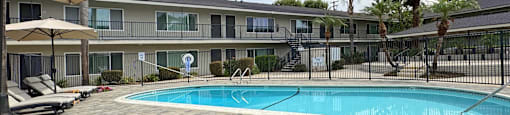A pool area with sun loungers and umbrellas in front of a building.