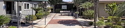 A leasing office is surrounded by greenery and a brick pathway.