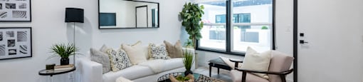 A modern living room with a white couch, a black and white mirror, a white fur throw, and a brown rug.