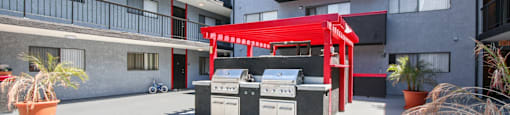 A red awning is over a grill and sink outside a building.