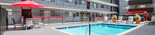 A swimming pool is surrounded by a patio with chairs and umbrellas.