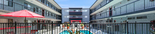 A pool area with red umbrellas and a potted plant in the foreground.