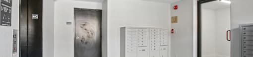 A room with a grey floor and white walls has a black door on the left and a white cabinet with drawers on the right.
