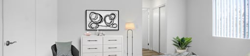 A bedroom with a bed, chair, and a white cabinet.