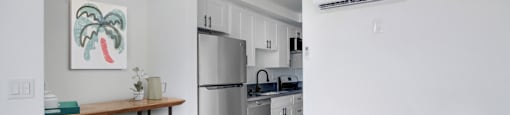 A kitchen with a refrigerator, a table, and a painting on the wall.