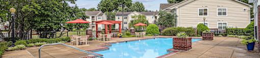 A pool surrounded by a concrete patio and a red umbrella.
