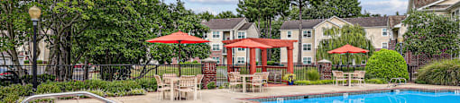 A swimming pool surrounded by trees and a red umbrella.