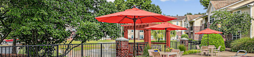 A poolside area with a table and chairs under a red umbrella.