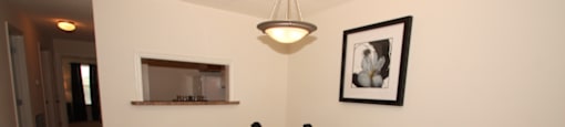 The furnished dining room has carpet throughout. There is a round wooden table with four black chairs positioned around it. There is a place setting for two on top of the table. There is a small breakfast bar that opens to the kitchen.