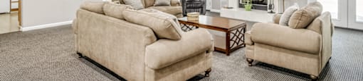 The clubhouse is furnished with two cream colored sofas, an oversized tan chair, a blue chair, and a dining room table with three chairs positioned around it.