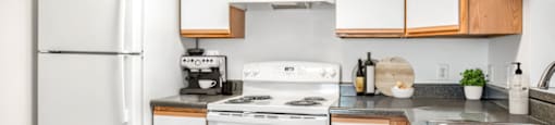 The vacant kitchen has white cabinets that feature natural wood-colored accents. Granite-style countertops throughout the space and a bar-top located just behind the stainless steel sink.