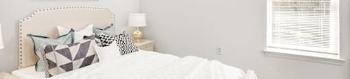 The vacant bedroom features tan carpet throughout with beige walls and a white textured ceiling. A window located on the right side of the room overlooks exterior trees. A rounded globe light sits in the center of the ceiling.