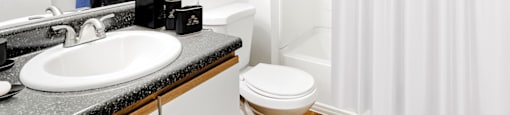 The bathroom also features a white shower/tub combo along with a black granite style bathroom vanity, white sink, and wood-colored trim surrounding the white cabinets